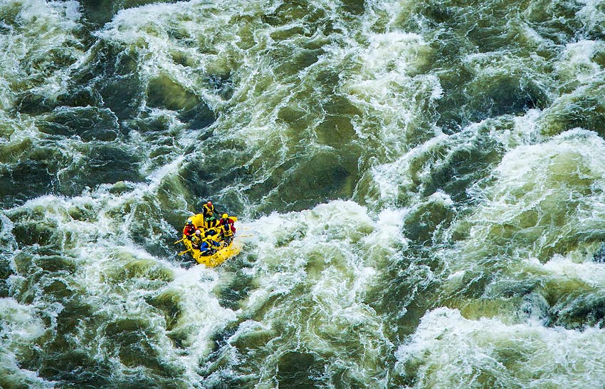 Un bote amarillo con seis personas a bordo parece pequeño desde la vista aérea de las olas de agua blanca. 